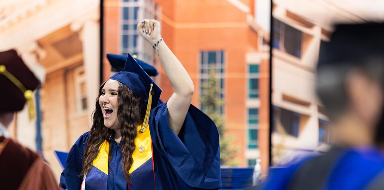 UNC graduate raising their arm and smiling during a graduation ceremony.